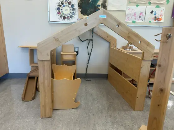 A wooden play-house frame in the Butterfly Room, with a rocking chair and wooden building materials